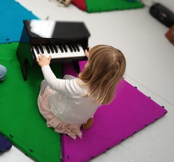 Deklica za otroškim klavirjem s prstki na tipkovnici.