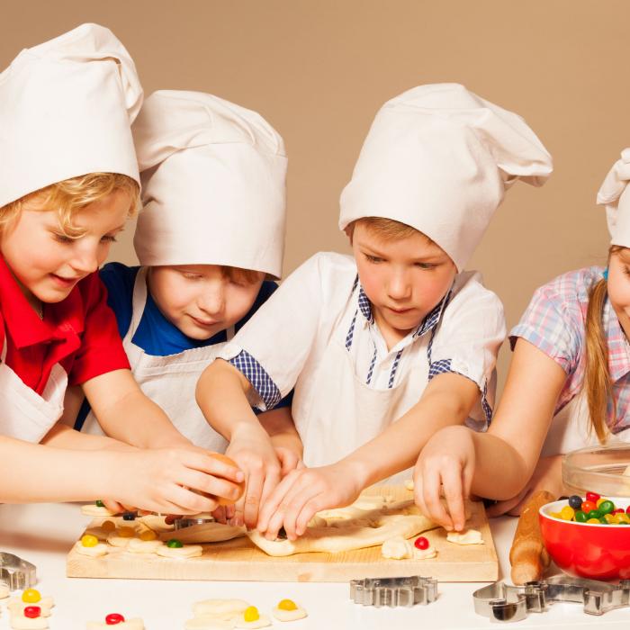 Otroci s kuharskimi kapami oblikujejo testo za piškote.