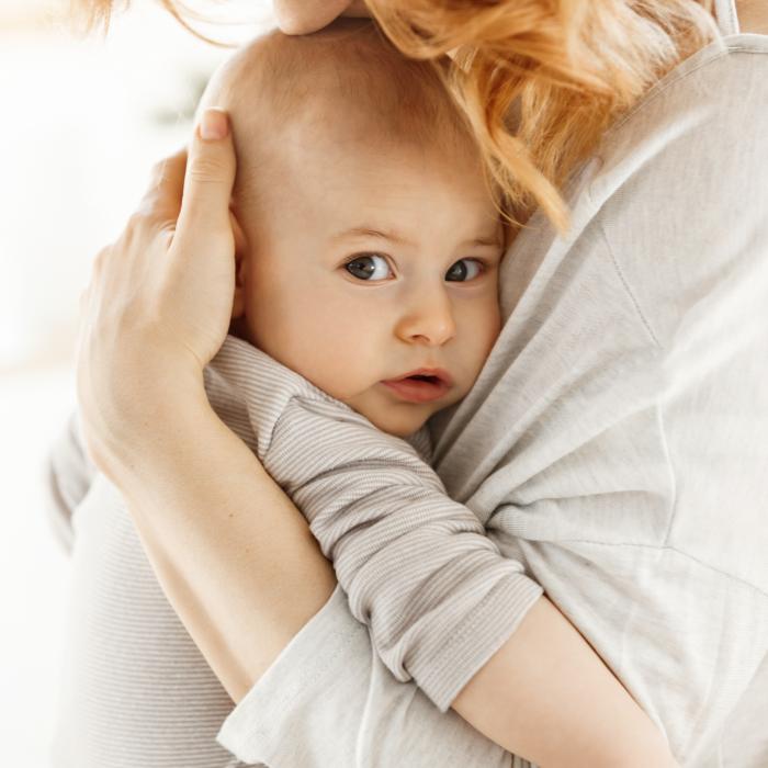 portrait sweet little child looking camera with interested expression while mother tenderly snuggle palming kissing her newborn baby