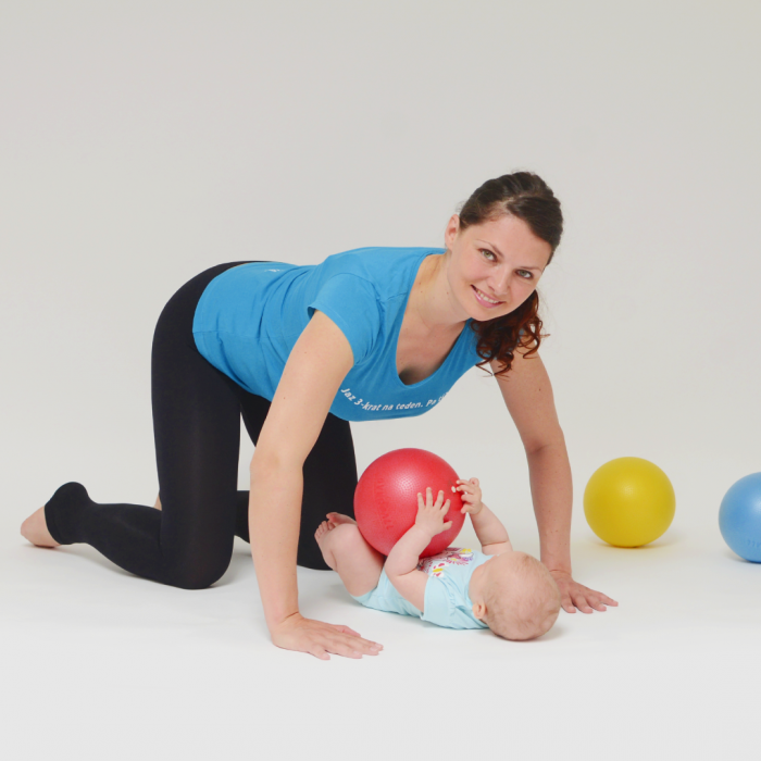 Mamica, sklonjena nad dojenčkom, med vadbo pilatesa.