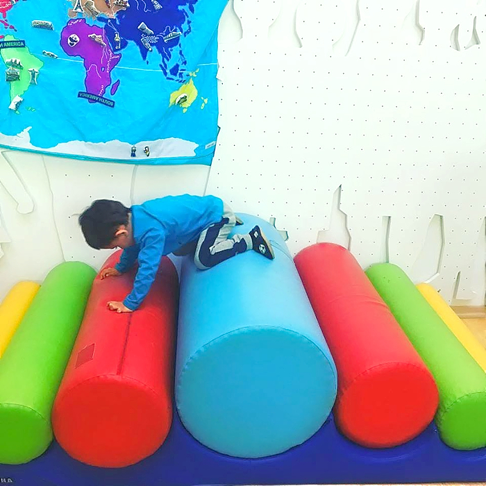 A child climbing on cylindrical cushions.