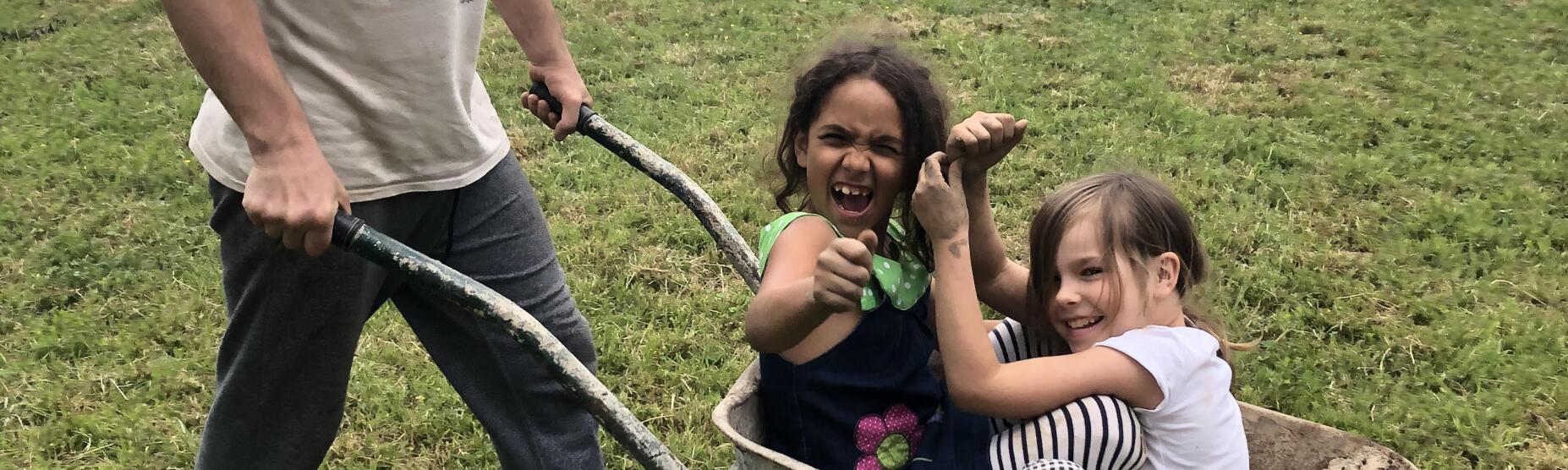 Deklici na vrtu v samokolnici, ki ju igrivo naokoli prevaža animator.