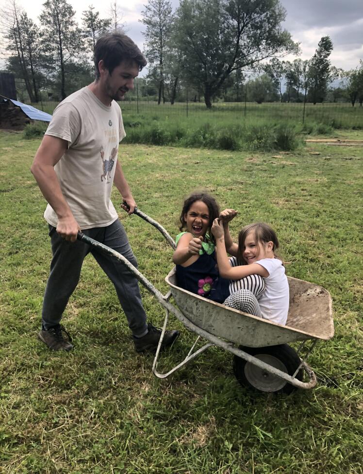 Deklici na vrtu v samokolnici, ki ju igrivo naokoli prevaža animator.