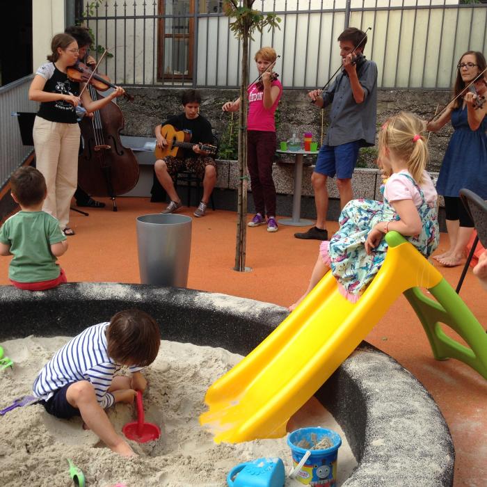 Otroci med igranjem na zunanjem igrišču ob poslušanju žive glasbe.