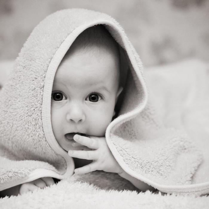 Črnobela fotografija dojenčka z brisačo na glavi.