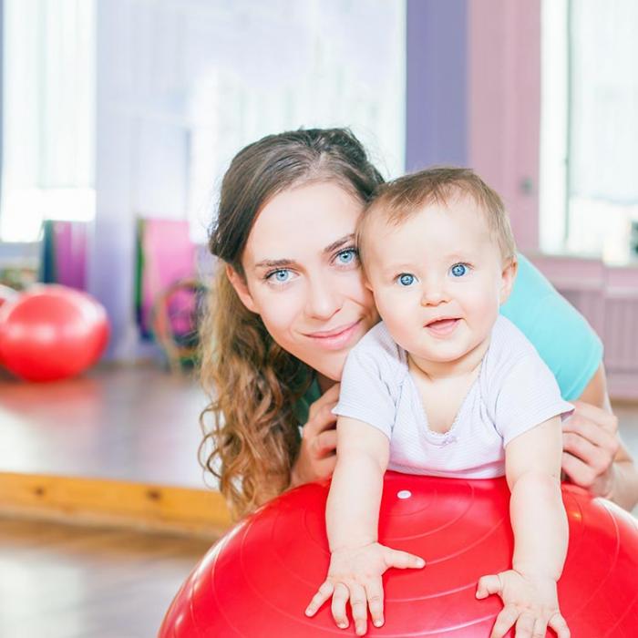 Mommy with a baby lying on a big ball.