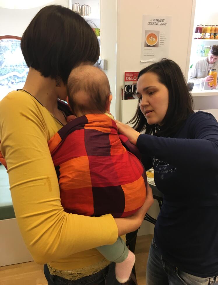 Mamica popravlja nosilno ruto drugi mamici z dojenčkom v ruti.