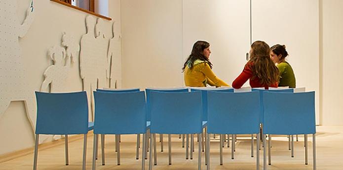 Animatorke Male ulice v sproščenem pogovoru v beli sobi z modrimi sedeži.