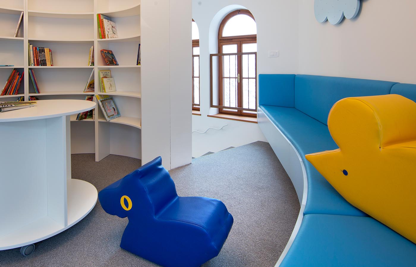Razgiban prostor z modro oblazinjeno klopjo in dobro založenimi knjižnimi policami.