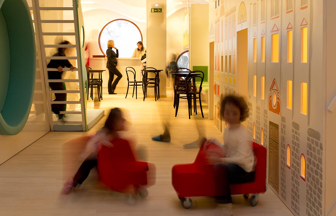Notranjost Male ulice s pisanimi stenami, rdečimi fotelji in razposajenimi otroci.