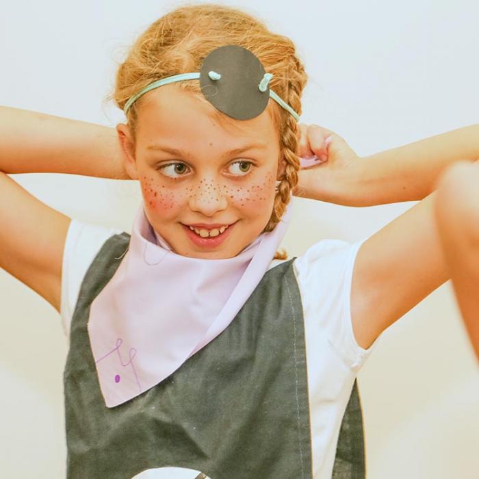 A young little pirate girl fixes a pirate blindfold.