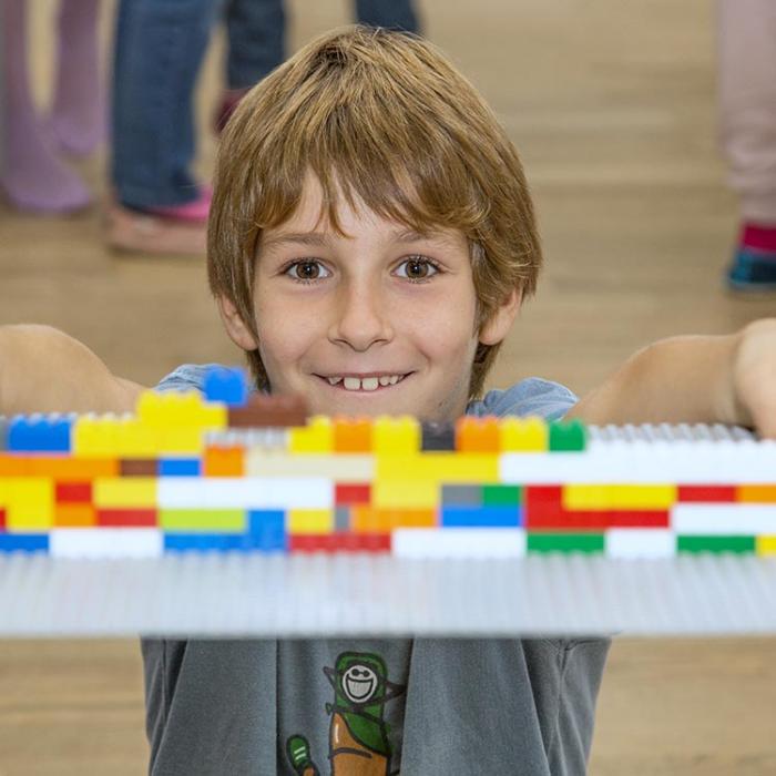 A boy with a colored wall made of Lego bricks.