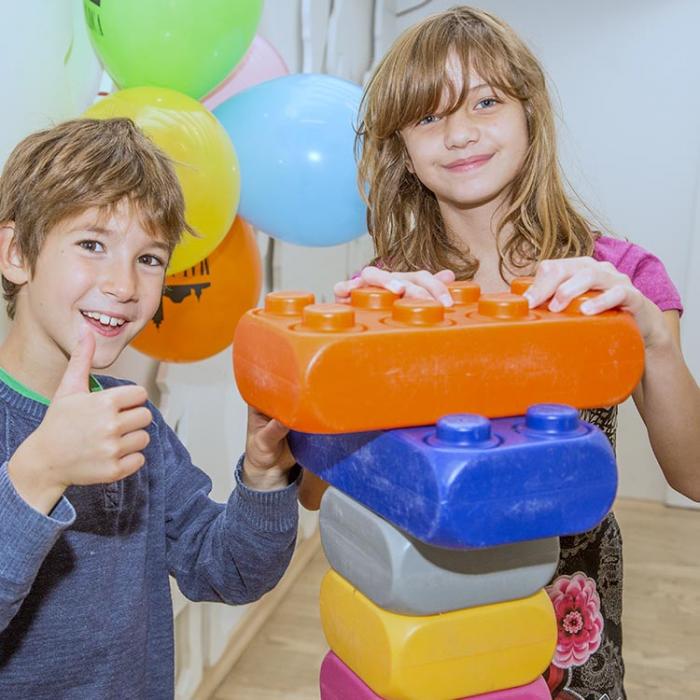 A boy and a girl pose next to a sculpture made of large Lego bricks.