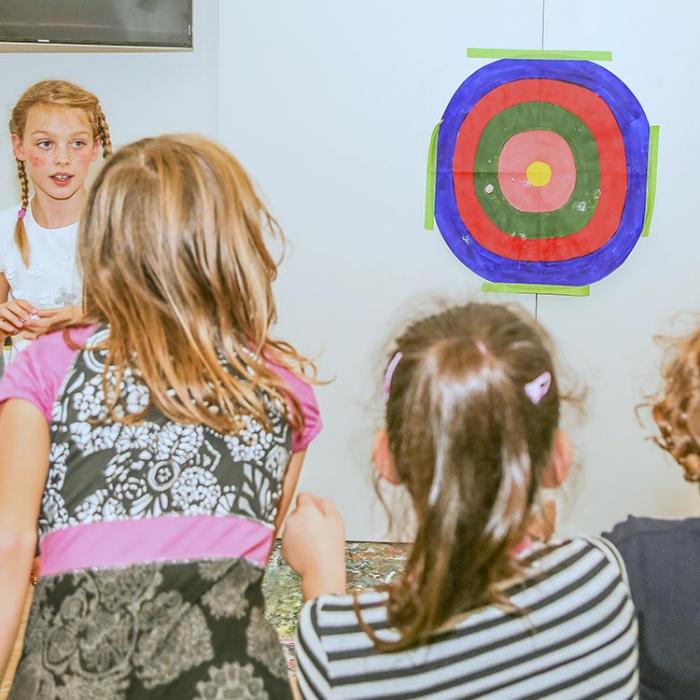 Kids at a party with a paper target on the wall in the background.