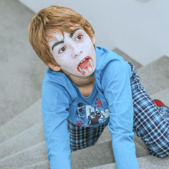 A boy with a vampire painting on his face.